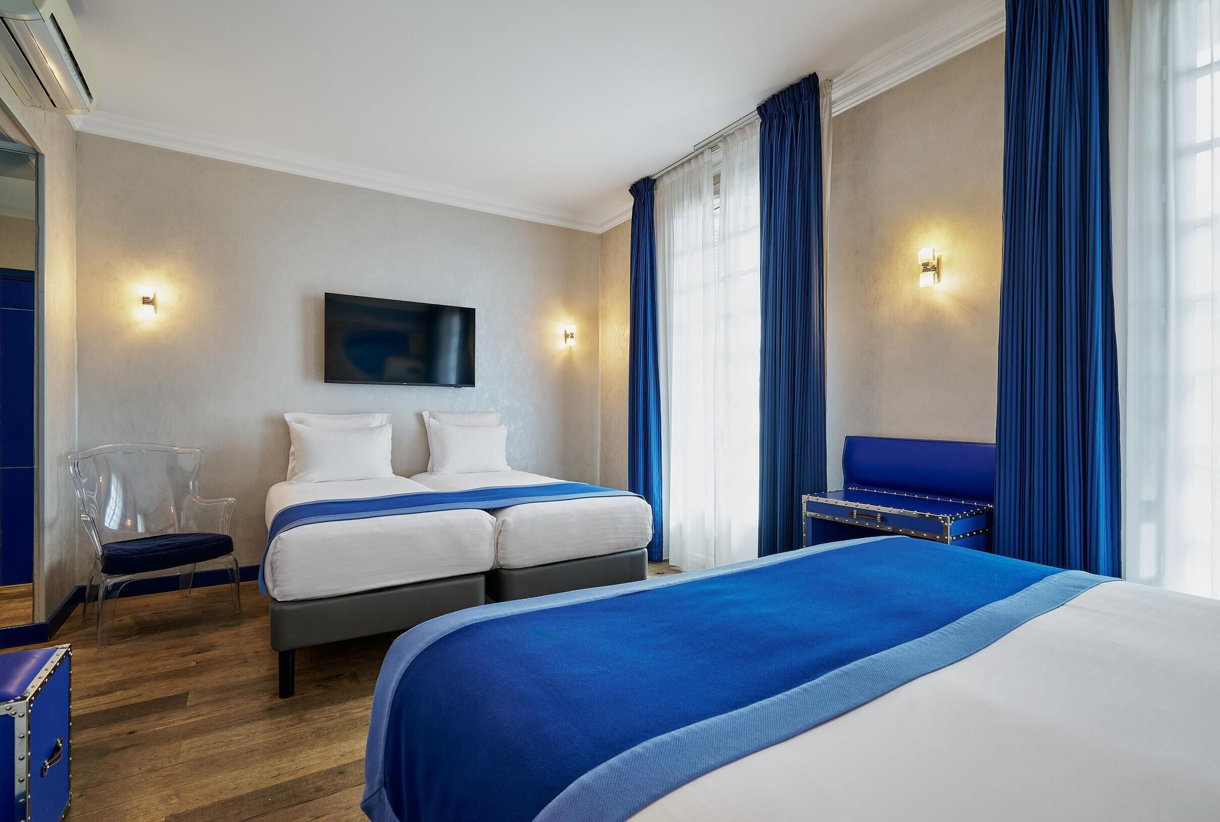 A hotel room with two beds, a TV mounted on the wall, and a seating area with a blue sofa.