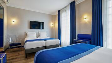 A hotel room with two beds, a TV mounted on the wall, and a seating area with a blue sofa.