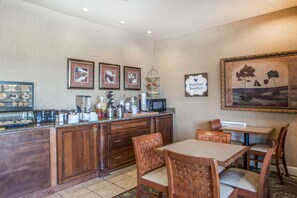 A kitchen with wooden cabinets, a microwave, and a coffee station. There are framed pictures on the wall and a sign that says "MainStart Breakfast."