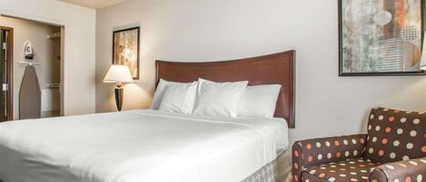 A hotel room with a large bed, a chair with polka dots, a painting on the wall, and a patterned floor.