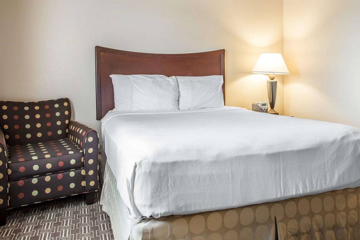 Una habitación de hotel con cama, una silla y una mesita de noche con lámpara.