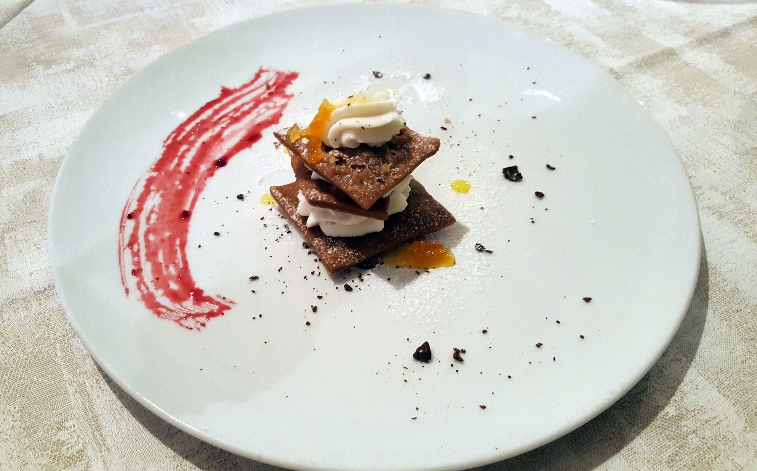 Un postre en un plato blanco con una mancha de salsa roja.