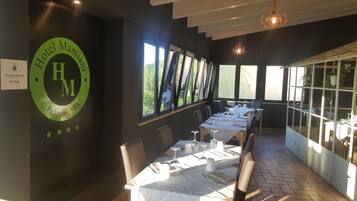 A restaurant with a long table set for dining, large windows with views, and a logo on the wall.