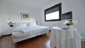 Ein modernes Hotelzimmer mit einem Einzelbett, einem kleinen Tisch mit Obstkorb, einem Flachbildfernseher und einem gerahmten Bild an der Wand.
