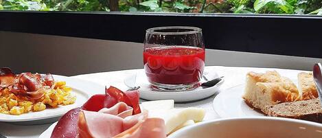 A breakfast setting with plates of food, a glass of red beverage, and a view of greenery through a window.