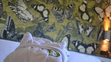 Een bed met een witte deken en een groen embleem, tegen een muur met een motief van vlinders.