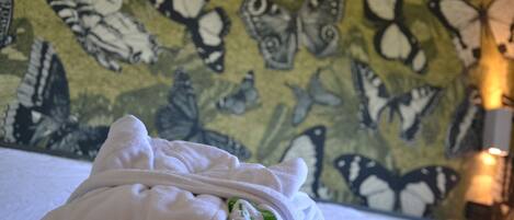 Una cama con una manta blanca y un emblema verde, frente a una pared con estampado de mariposas.