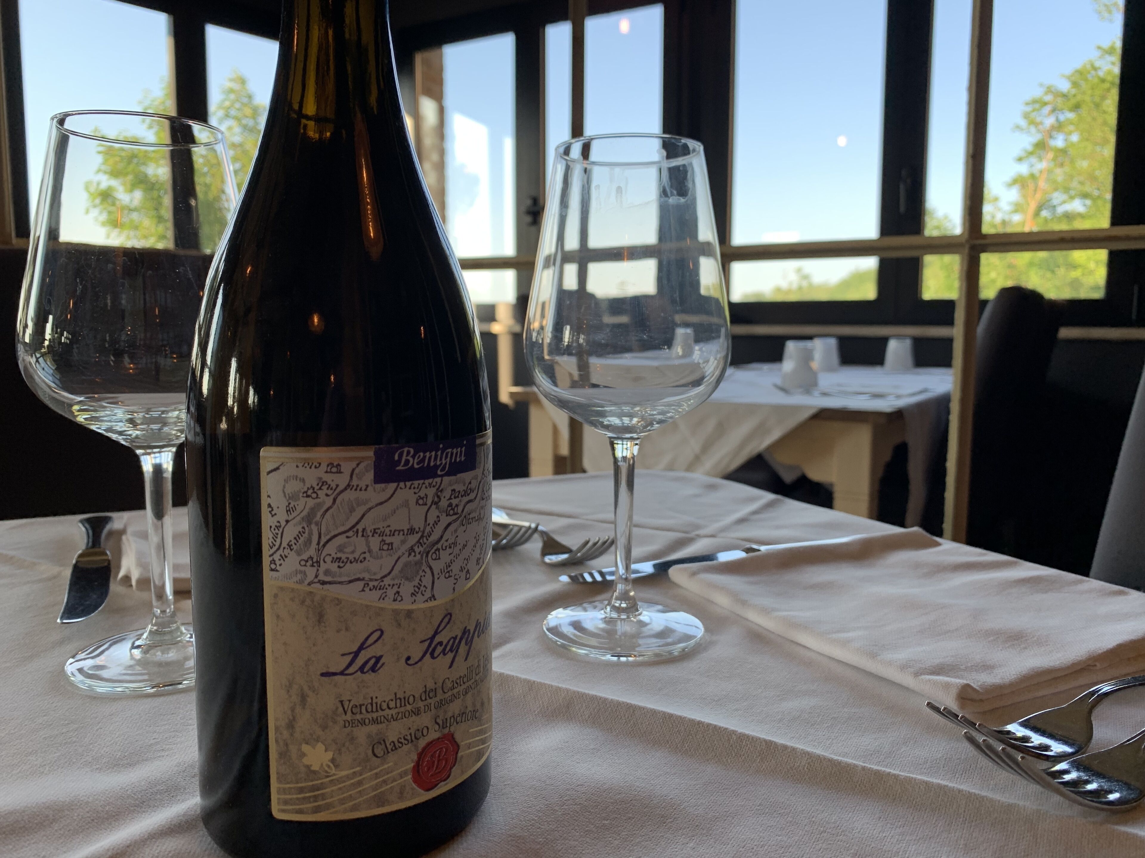 Une bouteille de vin avec une étiquette, deux verres à vin vides et une table dressée avec des couverts.