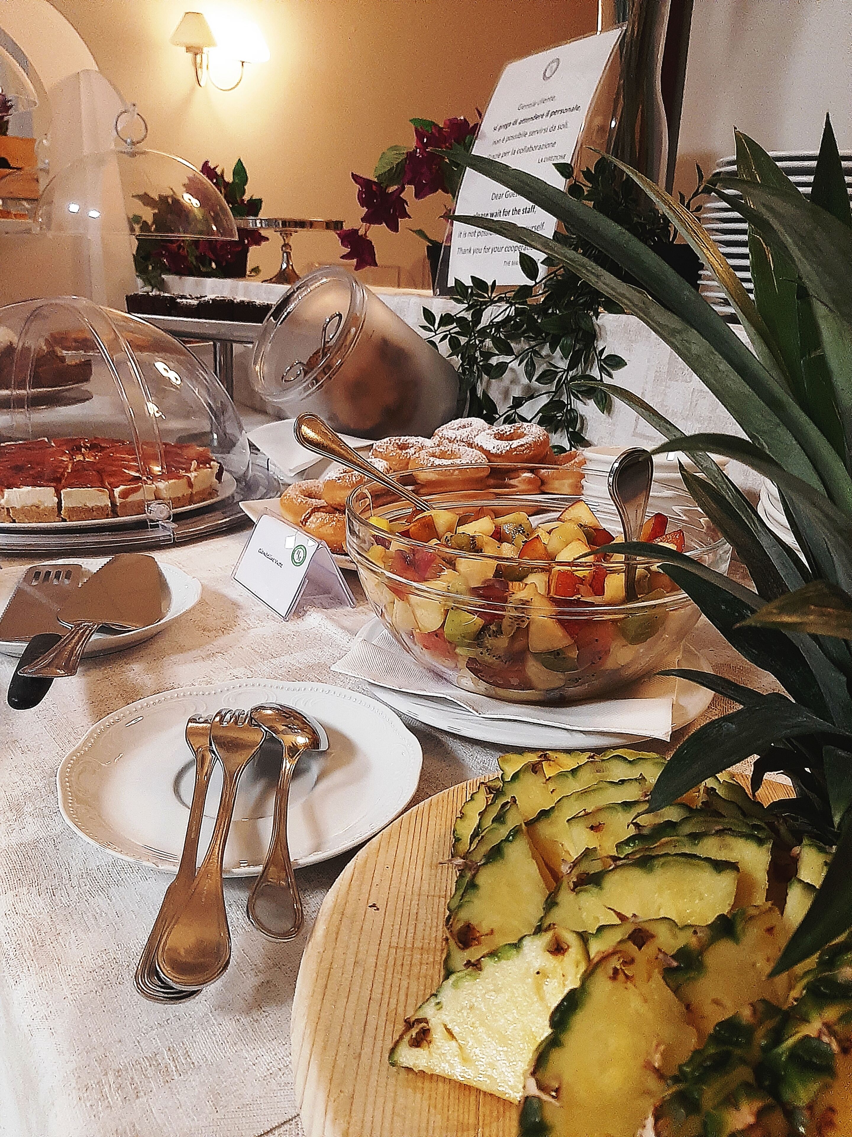 Una mesa de buffet con diversos platos, como una ensalada de frutas, un pastel y frutas cortadas.