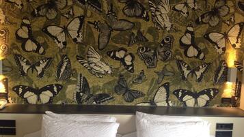 Habitación de hotel con una pared decorada con un estampado de mariposas. Dos almohadas blancas sobre la cama.