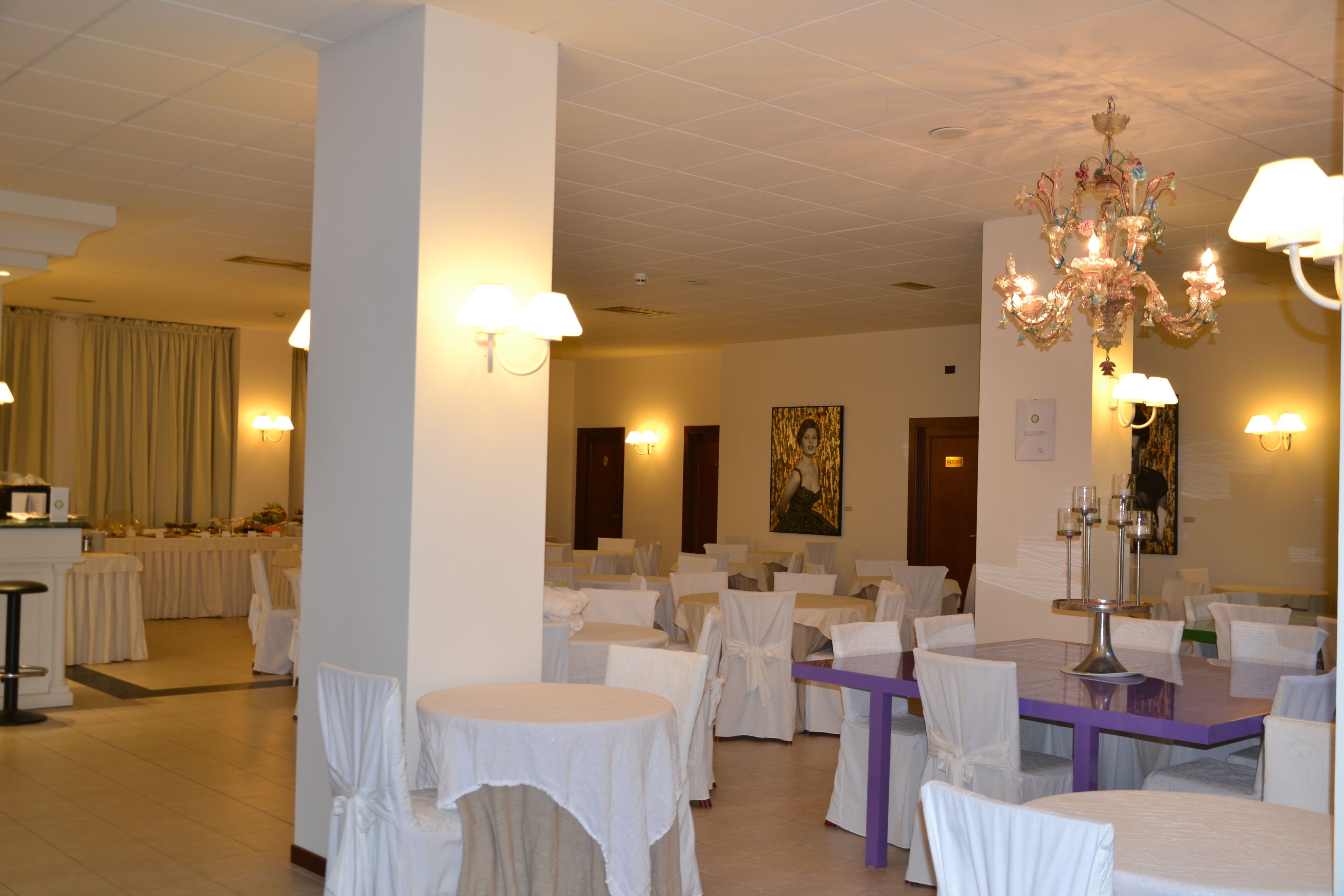 A banquet hall with round tables and chairs, a chandelier, and wall sconces.