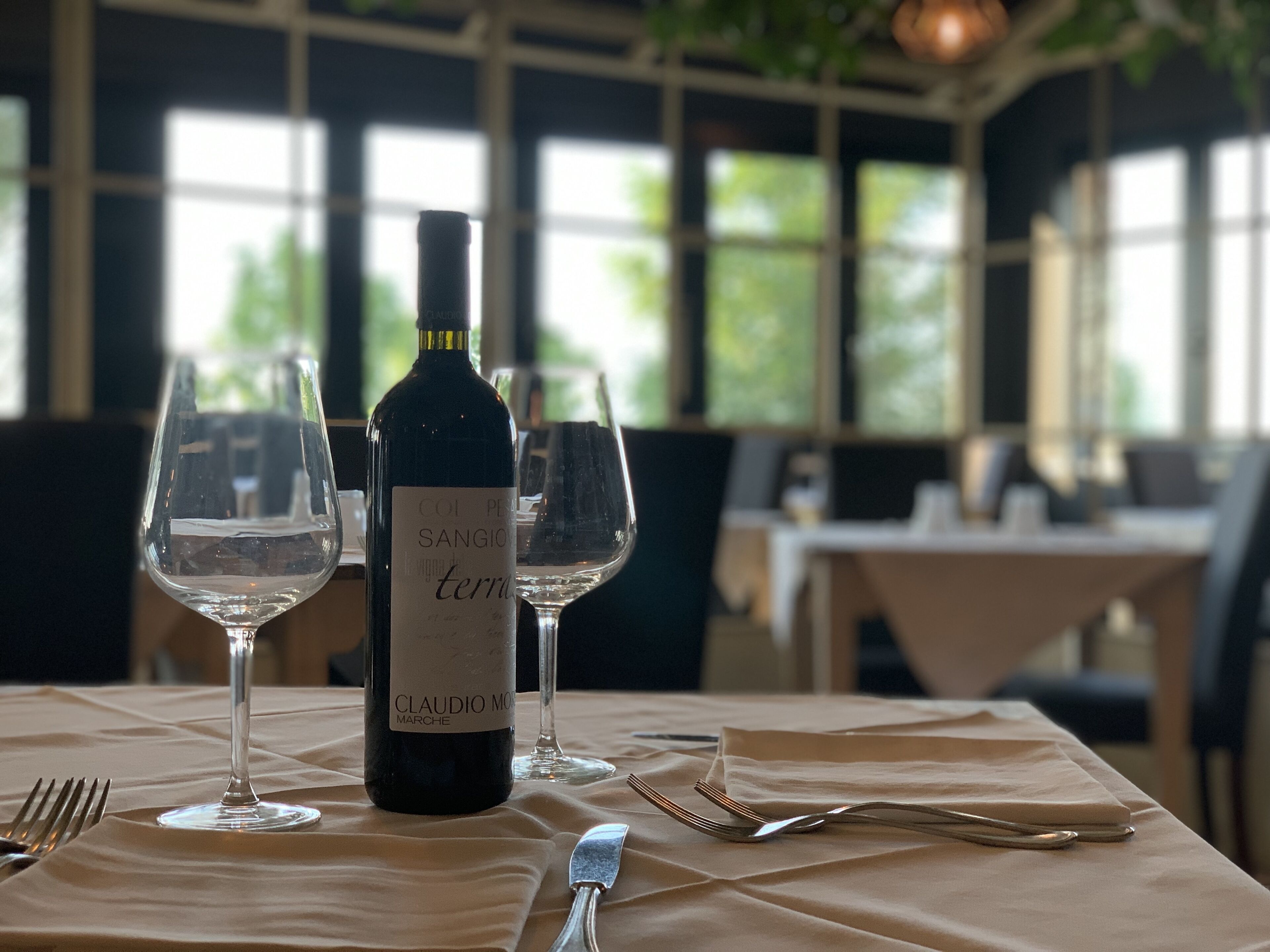 Una mesa servida con una botella de vino, dos copas de vino, un tenedor y un cuchillo.