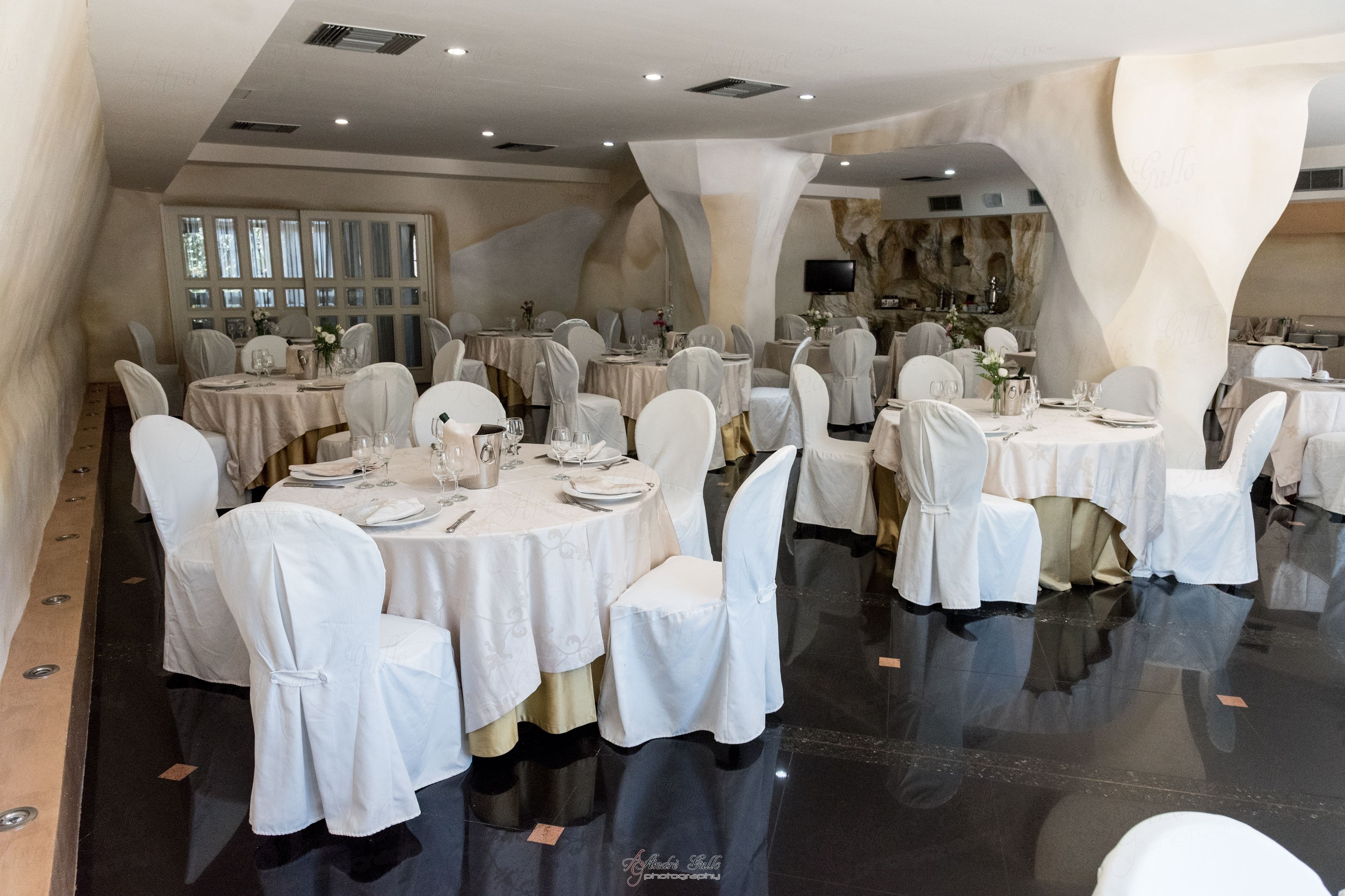 Une salle de banquet avec des tables rondes, des nappes blanches et des chaises recouvertes de housses blanches.
