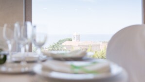 A dining table with plates and glasses, a chair, and a view of a building with a tower through a window. - Hotel Residence Arcobaleno (Palmi)