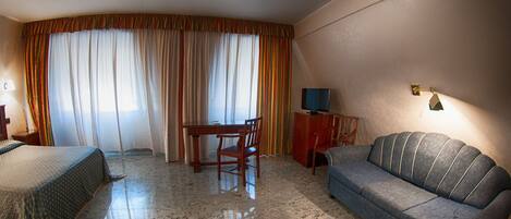 Habitación de hotel con cama, sofá, mesa de comedor con sillas, televisor y lámpara.