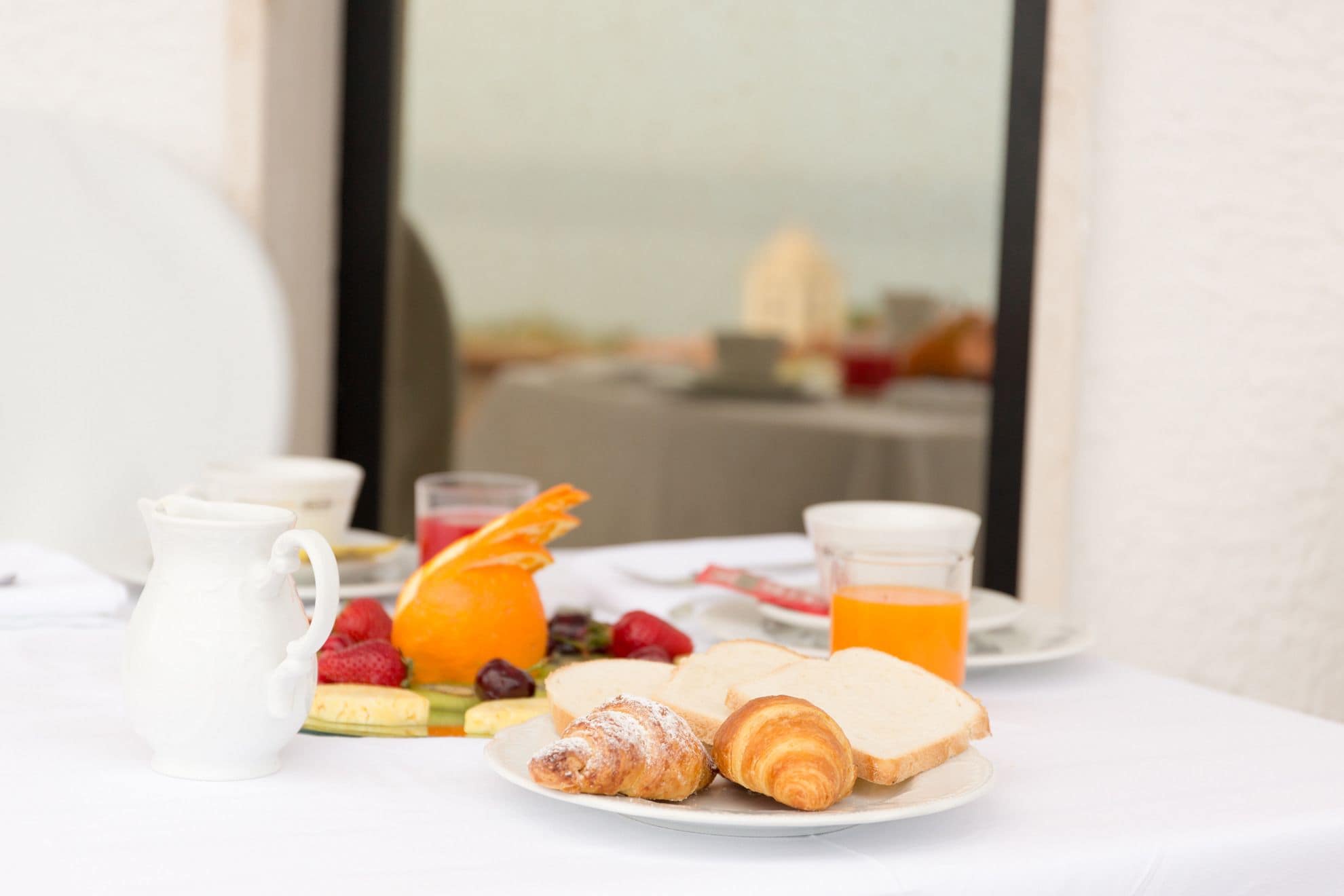 A breakfast table with croissants, bread, fruit, and orange juice.
