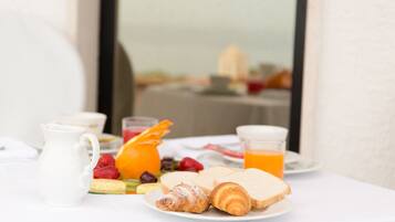 A breakfast table with croissants, bread, fruit, and orange juice.
