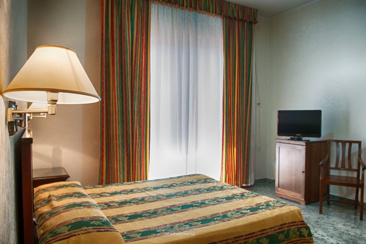 Una habitación de hotel con cama, escritorio con televisor, una silla y una lámpara.
