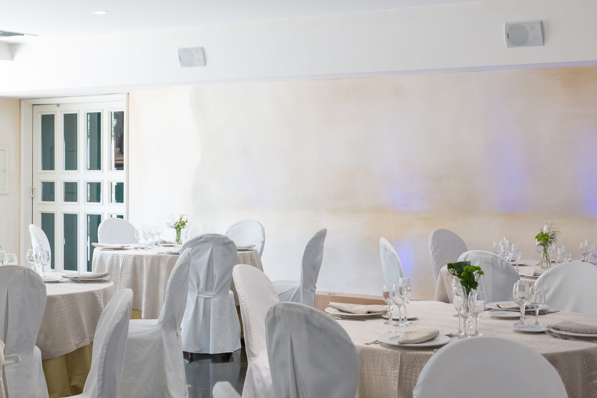Un salón de banquetes con mesas redondas dispuestas para comer, sillas blancas y un amplio ventanal con vistas.