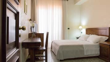 A hotel room with a bed, a desk with a lamp, a chair, and a nightstand with a lamp.
