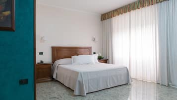 Habitació d'hotel amb llit, una vetust i una làmpada, llum penjada a la paret, i finestra amb cortines.