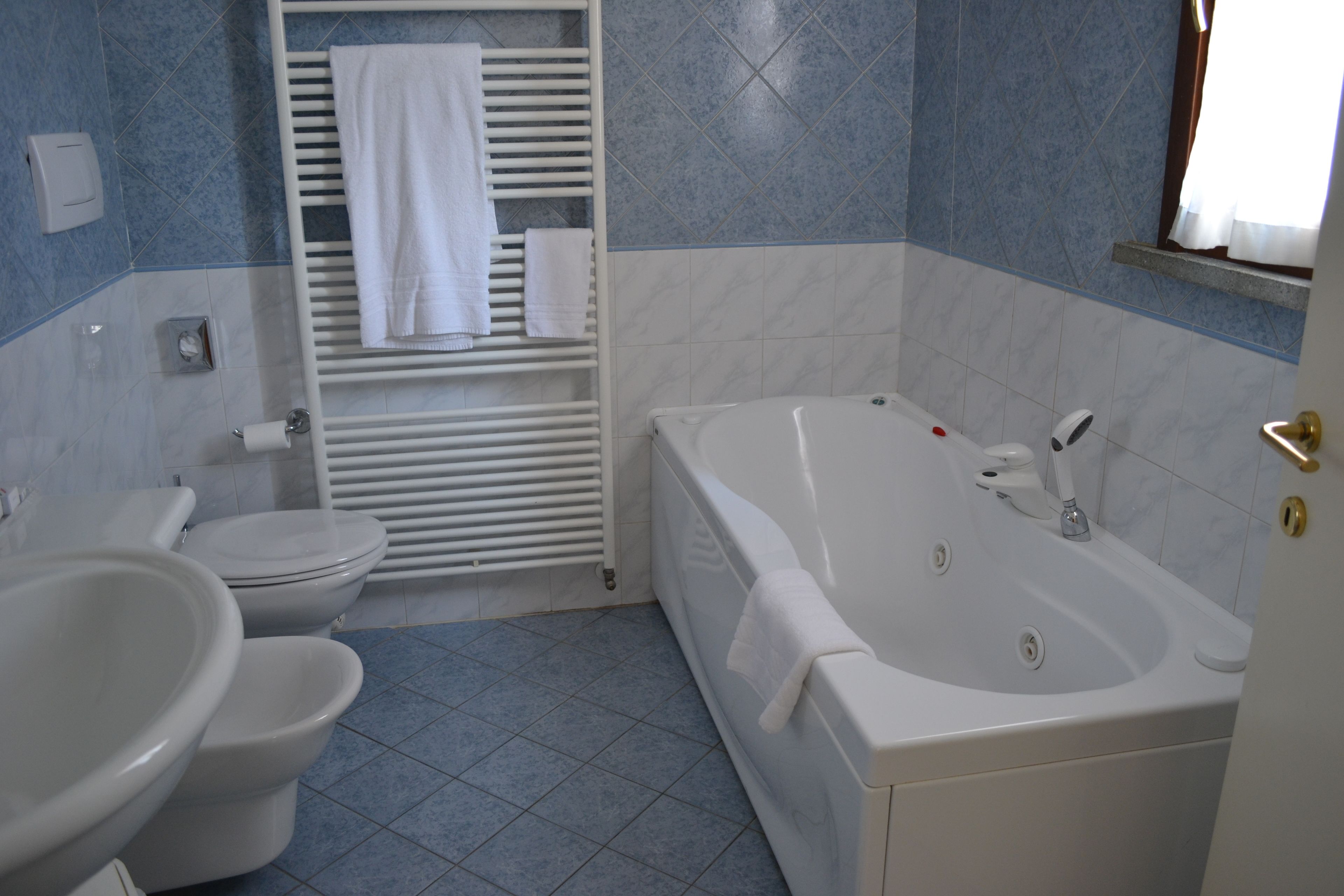 Une salle de bain avec une baignoire, deux toilettes, un bidet et un porte-serviettes.