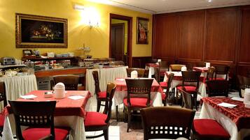 A dining area with tables set for service, chairs with red cushions, and a buffet line with various food items.
