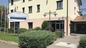 Een hotelschild met de tekst 'TRICOLOR HOTEL', omringd door groen en een verharde oprijlaan.