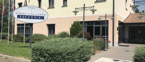Ein Hotel-Schild mit der Aufschrift "TRICOLOR HOTEL", umgeben von Grünpflanzen und einem gepflasterten Eingang.