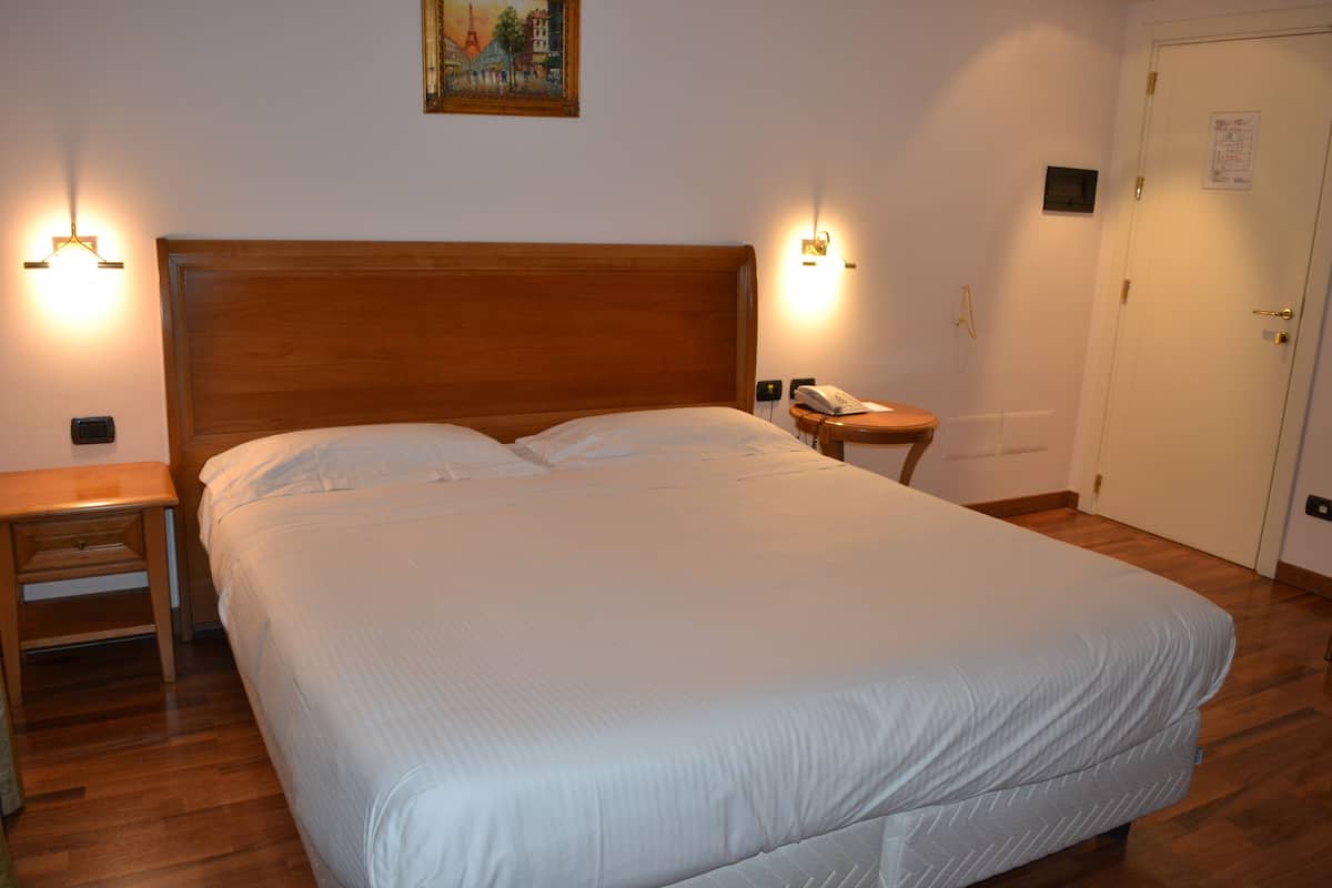 A neatly made bed with a wooden headboard, two bedside lamps, a nightstand, and a door with a lock.