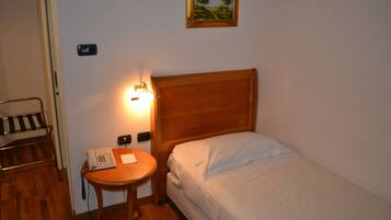 A small, neatly arranged bedroom with a wooden headboard, a bedside table with a telephone, a lamp, and a framed picture on the wall.