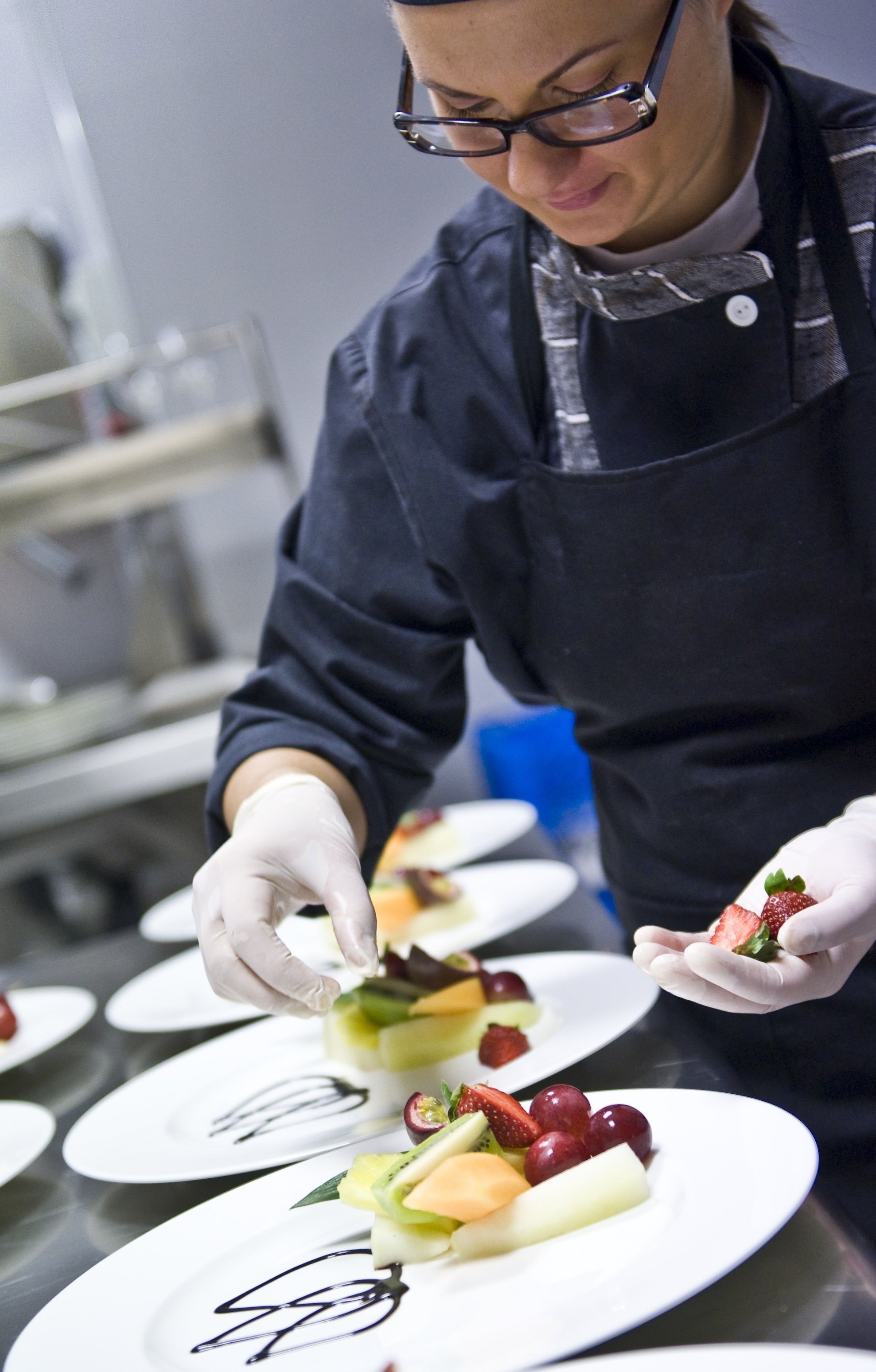 A chef preparing a dish with strawberries and other fruits on a white plate.