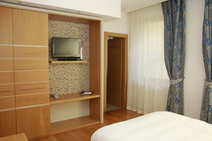 Habitación de hotel con armario de madera, televisor en estante, cama y puerta que da a otra habitación.
