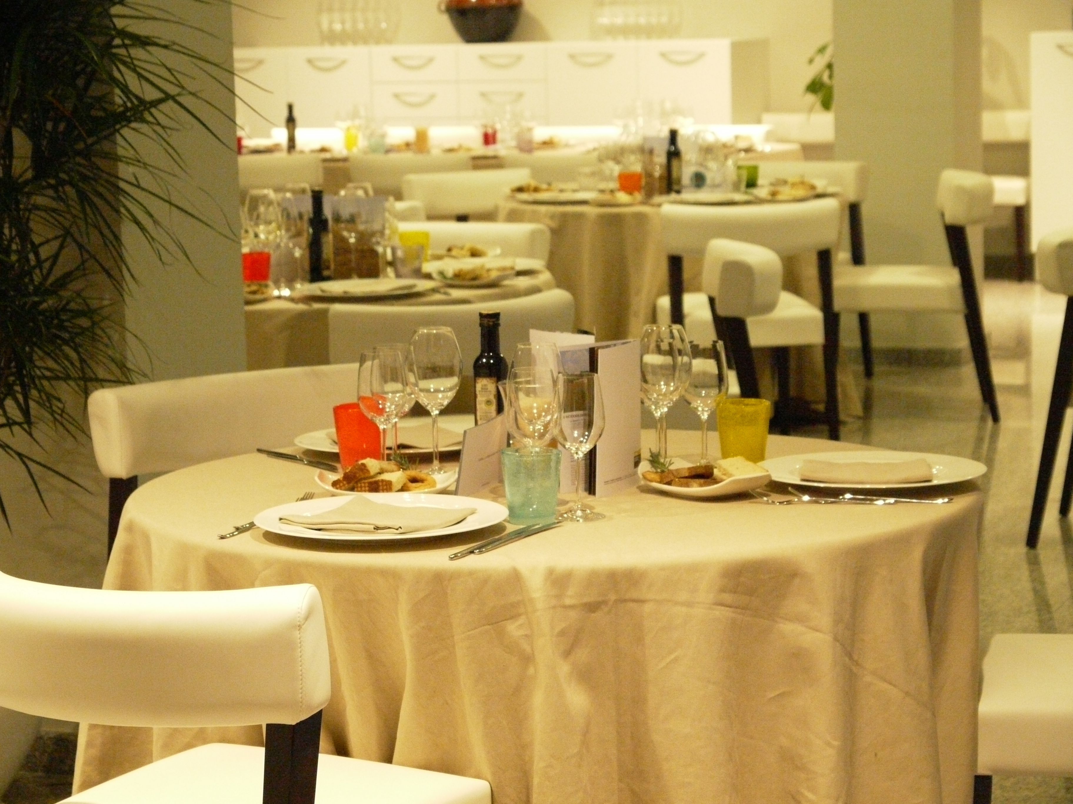 Un comedor con mesas redondas dispuestas para una comida, cada una con platos, cubiertos y vasos.