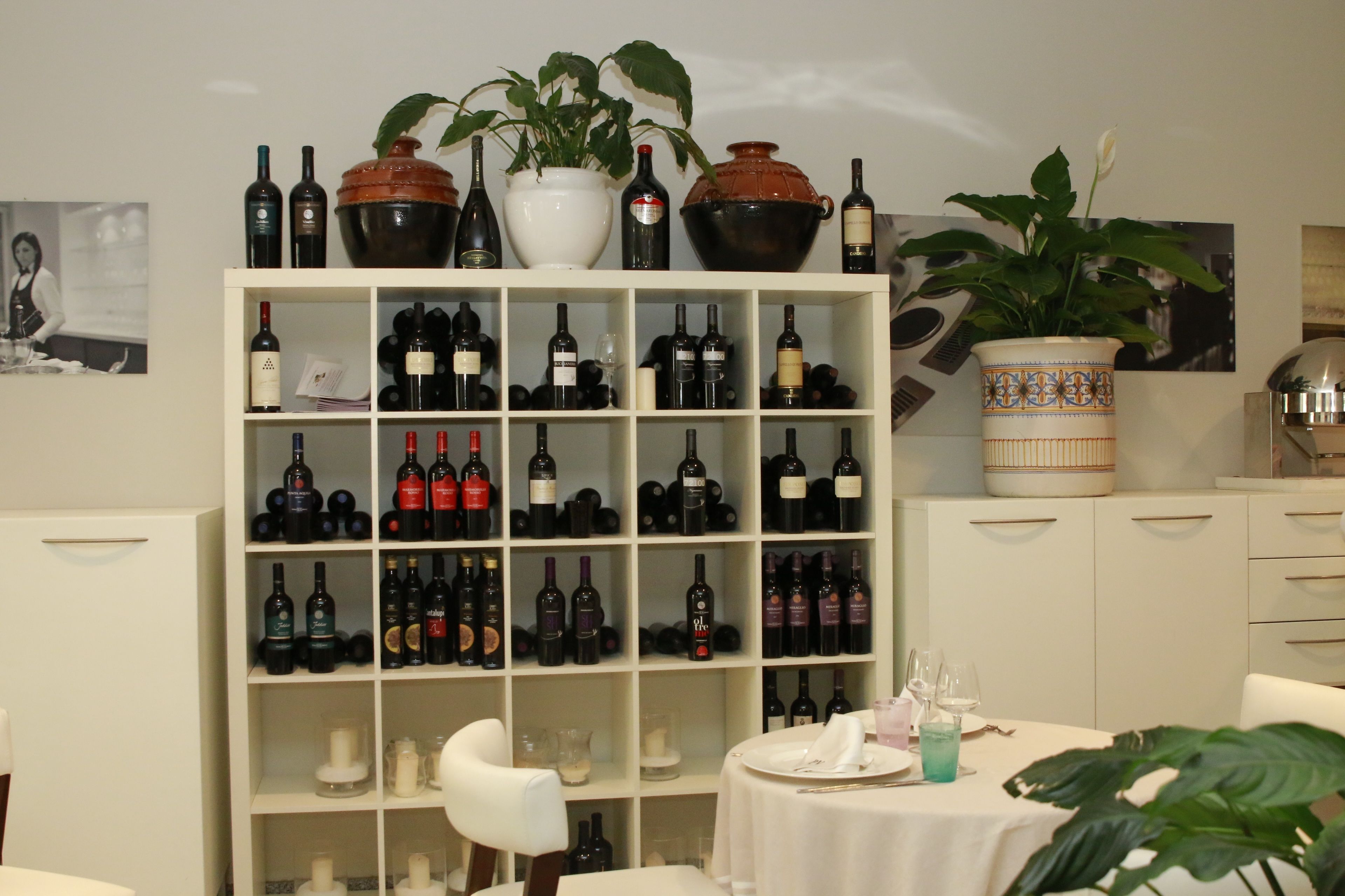 Una bodega con estantes llenos de botellas de vino, una mesa de comedor con sillas y plantas decorativas.