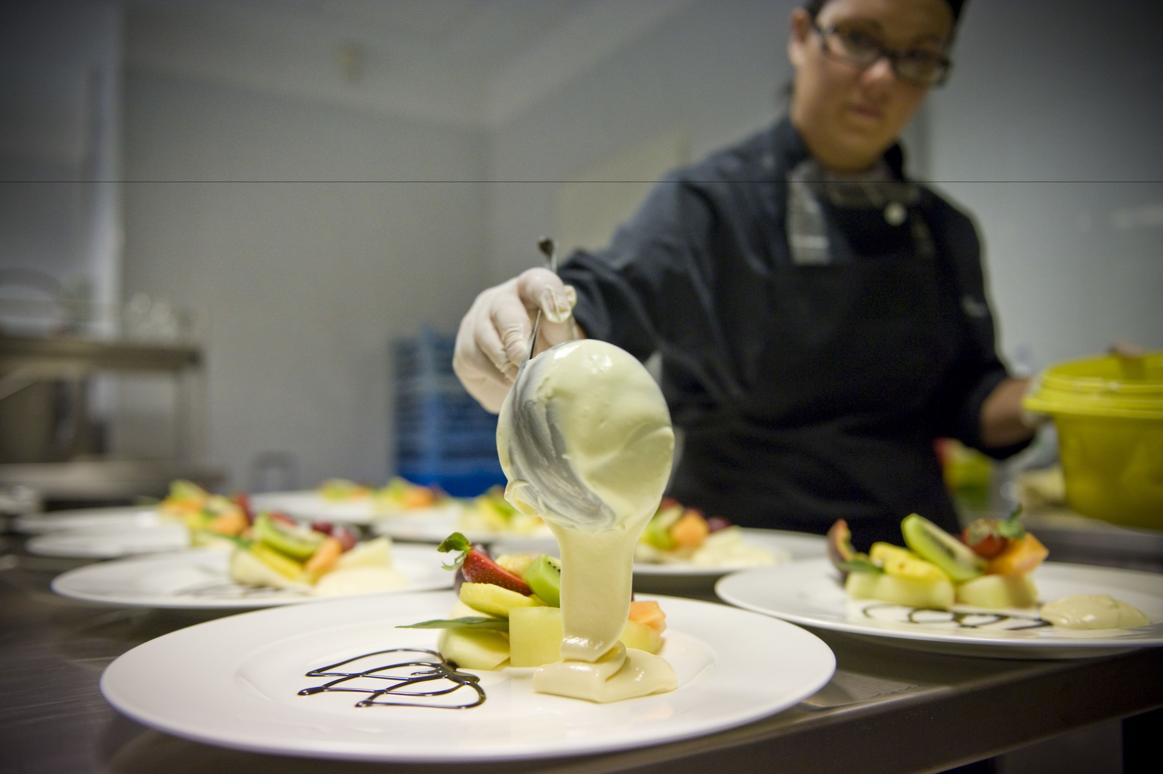A chef preparing a dessert with a creamy sauce on a plate with fruit.