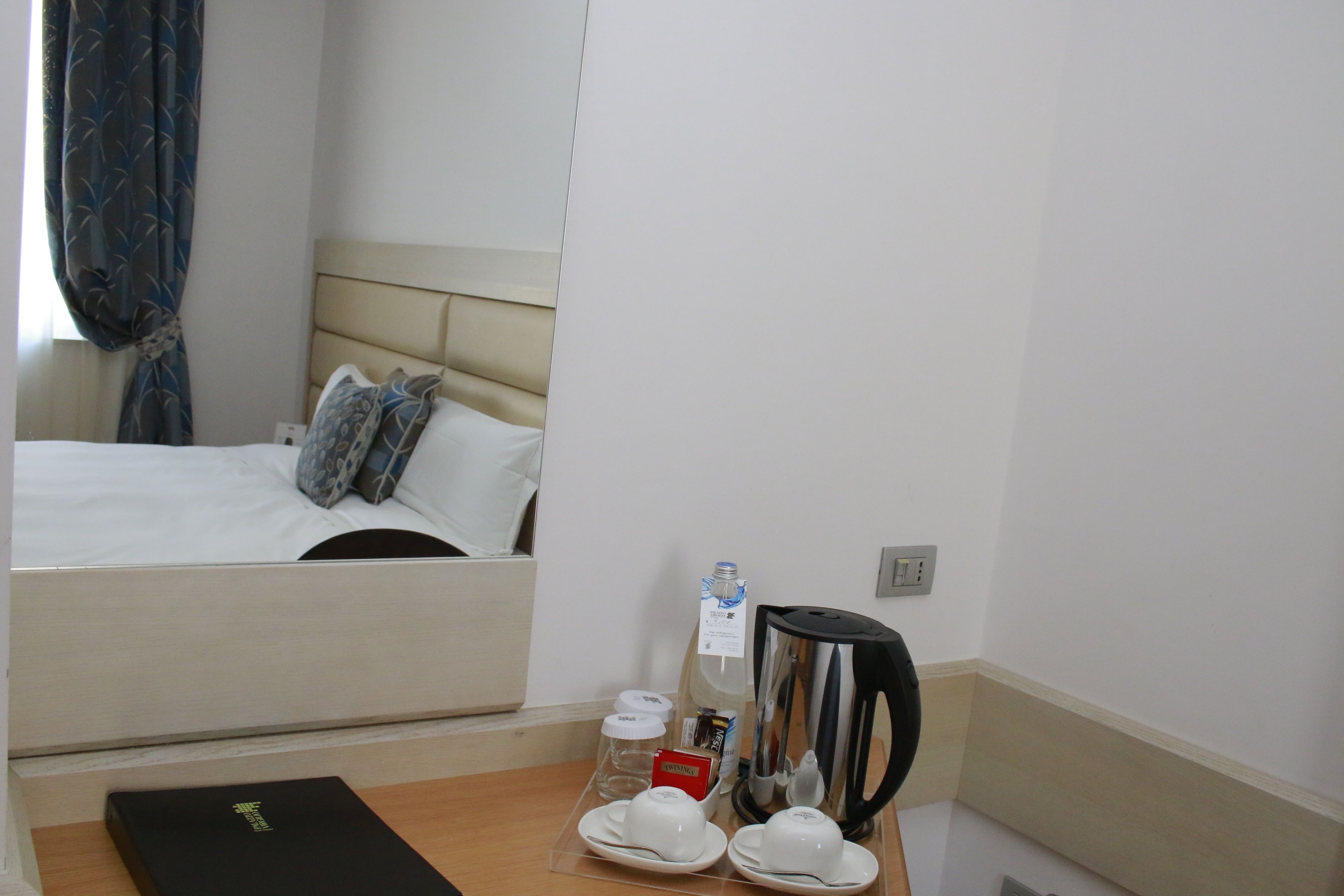 Una habitación de hotel con cama, mesita de noche, cafetera, tazas y una botella de agua.