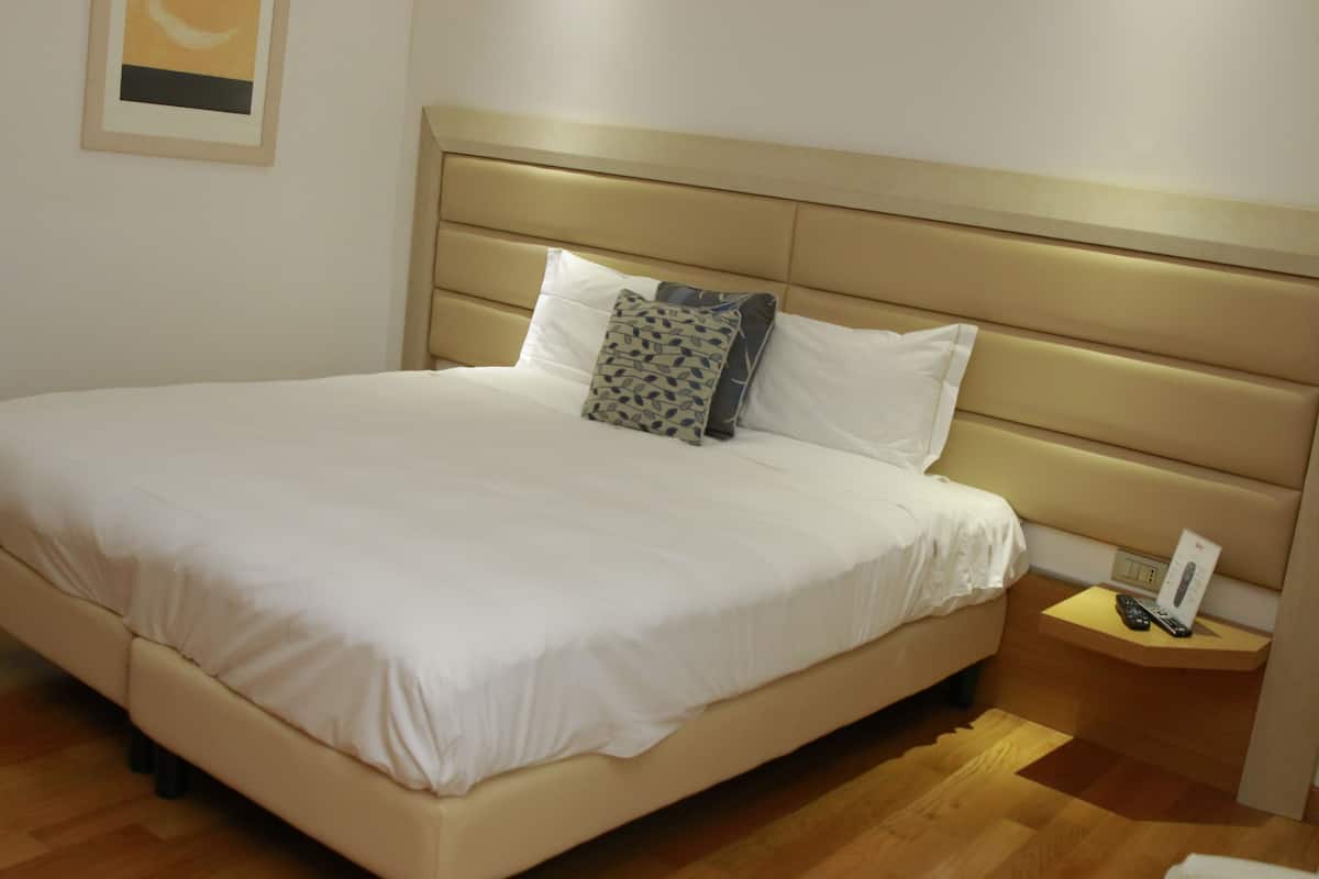 A neatly made bed with a headboard, a bedside table with a remote control, and a framed picture on the wall.
