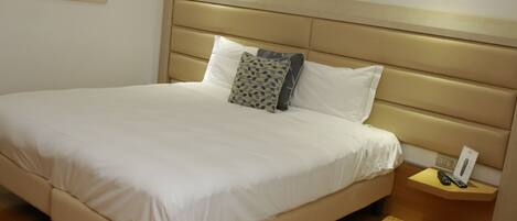A neatly made bed with a headboard, a bedside table with a remote control, and a framed picture on the wall.