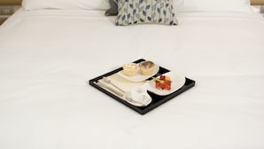 A neatly made bed with white linens, a tray with breakfast items, and a patterned pillow. - Palazzo Virgilio (Brindisi)