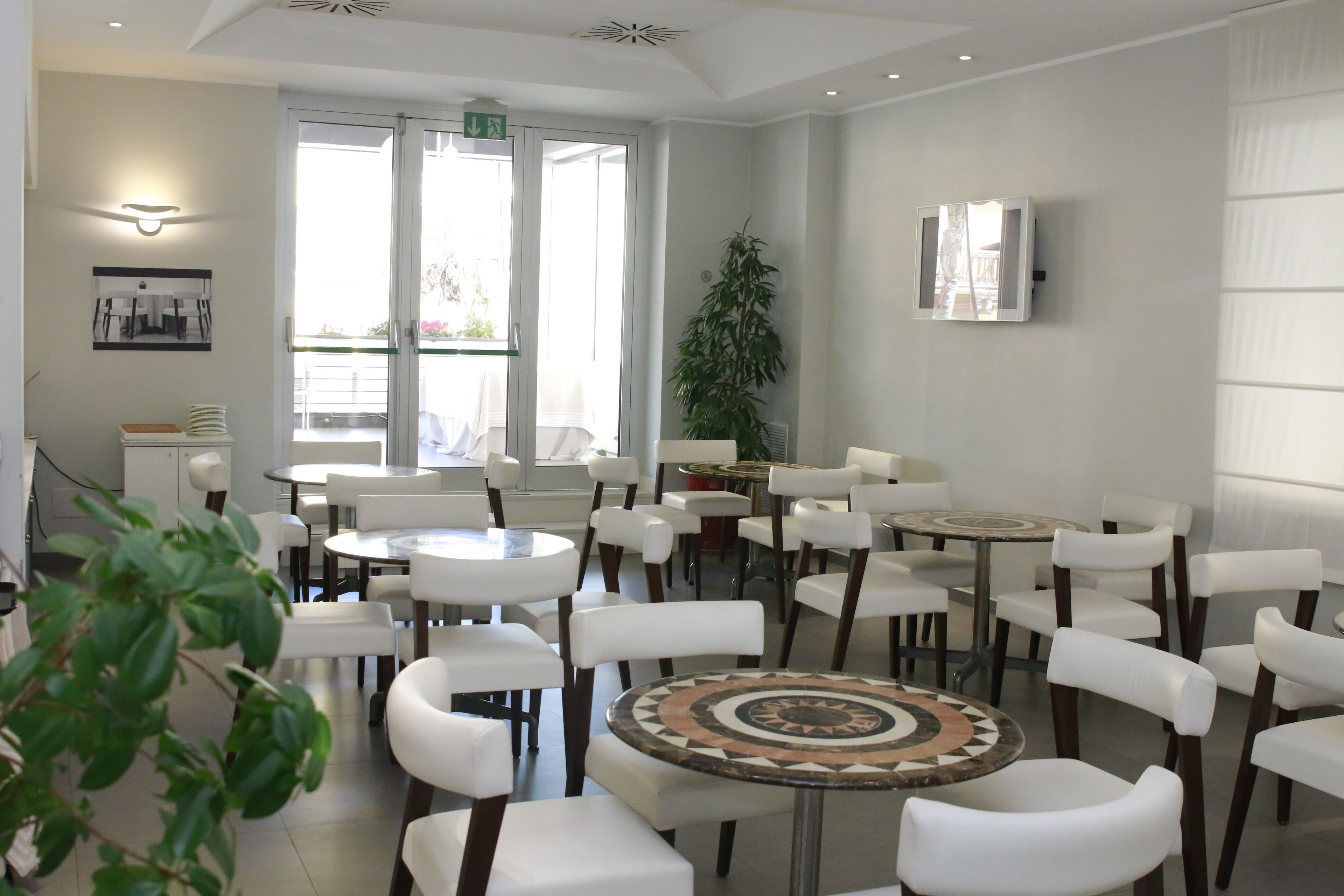A modern dining area with round tables and white chairs, large windows, and a potted plant.