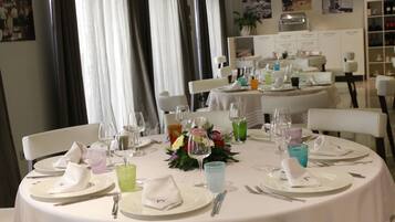 A dining table set for a meal with white tablecloths, neatly arranged plates, glasses, and cutlery.