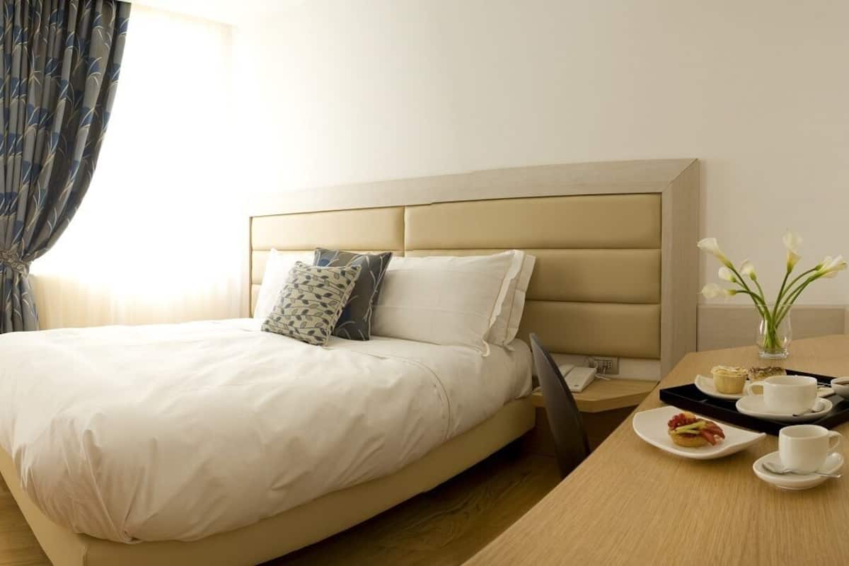 A hotel room with a bed, a chair, a desk with a tray of breakfast items, and a TV on a shelf.