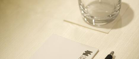 A clear glass bottle with a white label, a black pen, and a white envelope on a wooden surface.