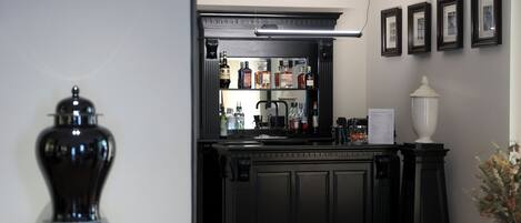 Zona de bar con una barra de madera oscura, estantes con botellas y un jarrón blanco.