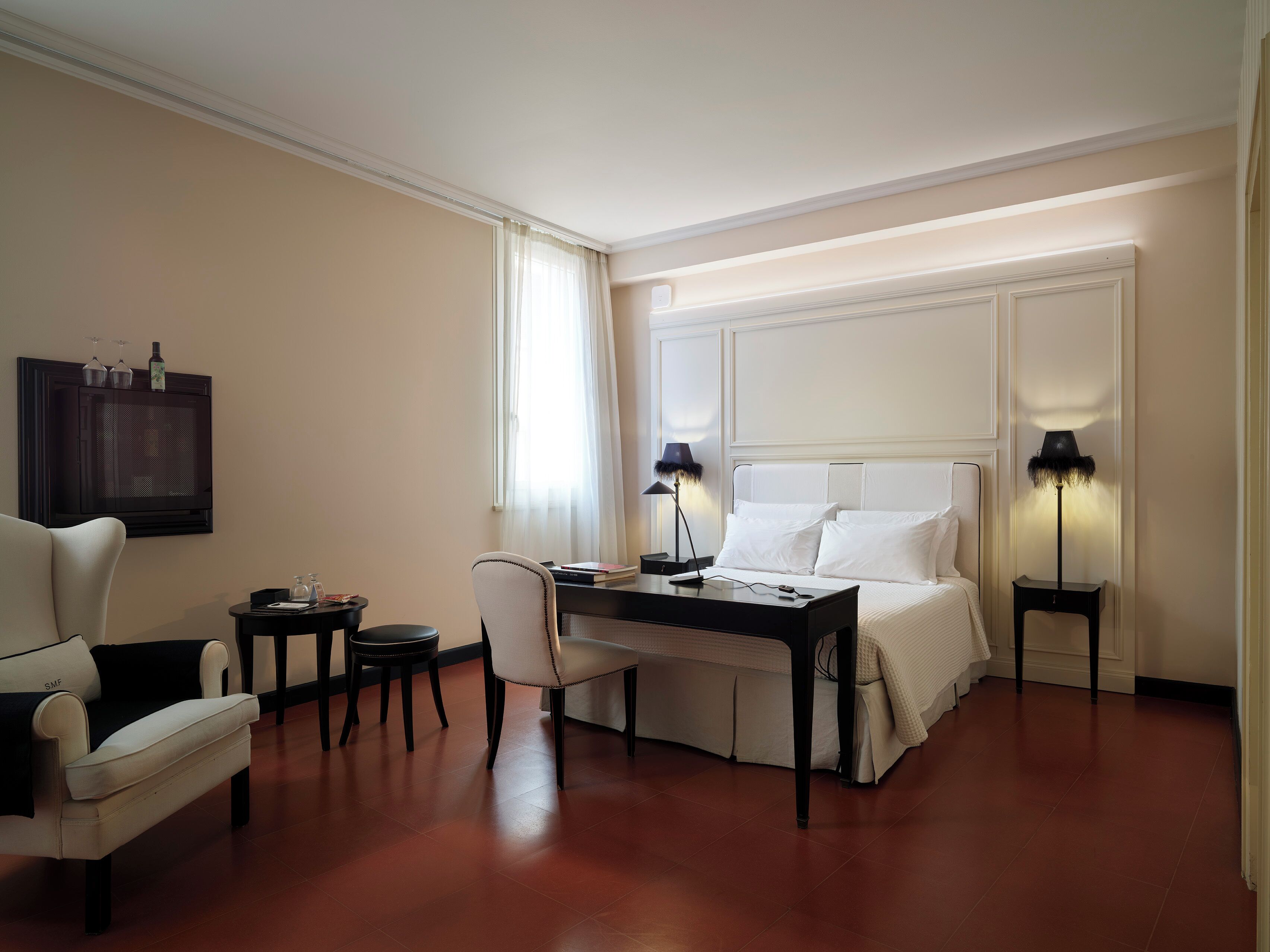 A hotel room with a bed, a desk, a chair, a TV, and two bedside lamps.