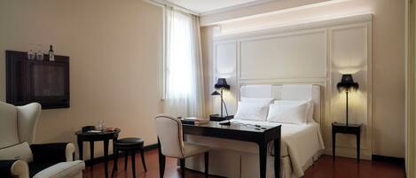 A hotel room with a bed, a desk, a chair, a TV, and two bedside lamps.
