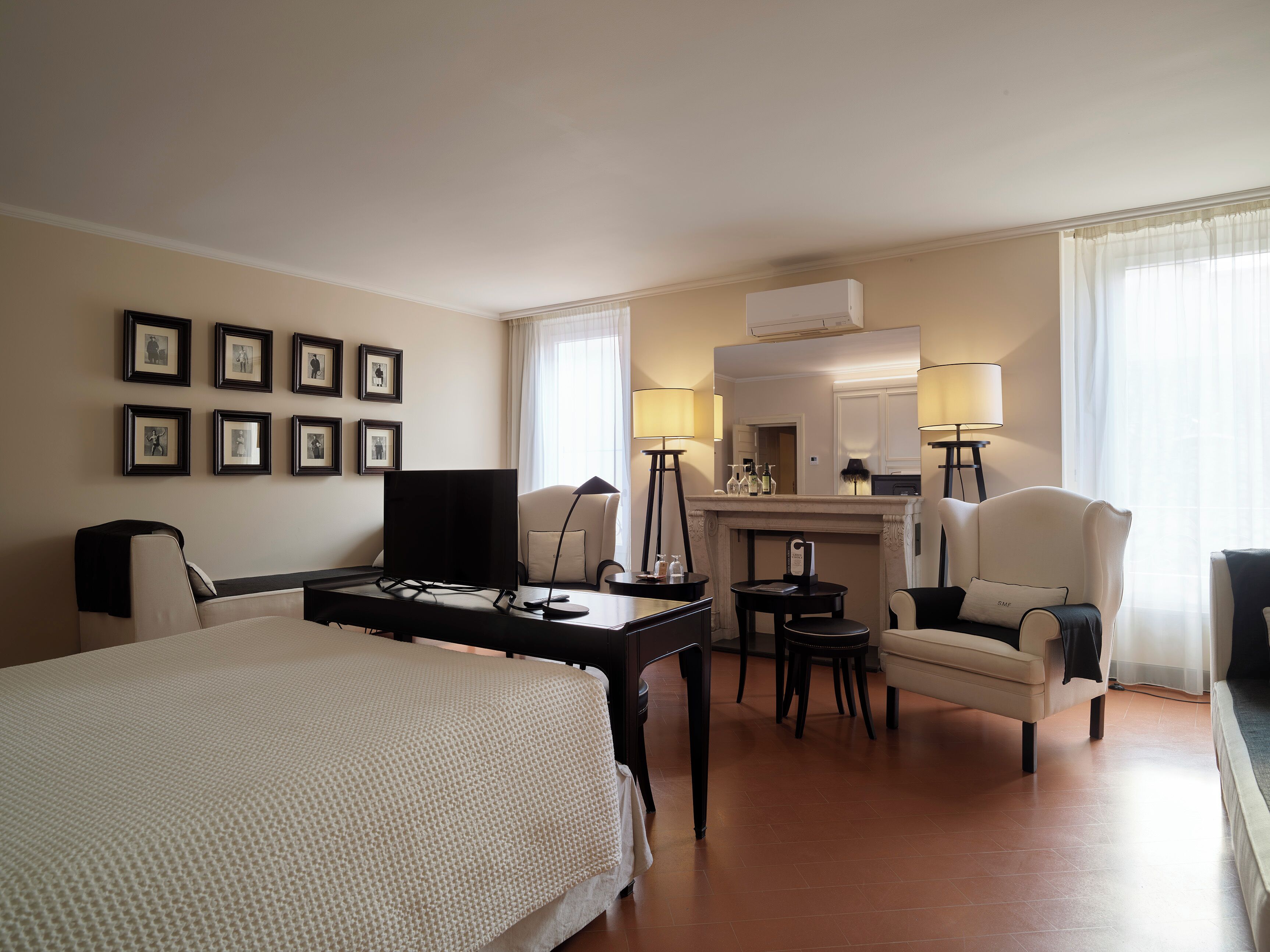 A hotel room with a bed, desk, chair, fireplace, and framed pictures on the wall.