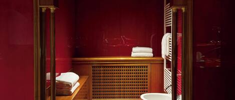 A modern bathroom with a red wall, a wooden vanity, a toilet, and a sink.