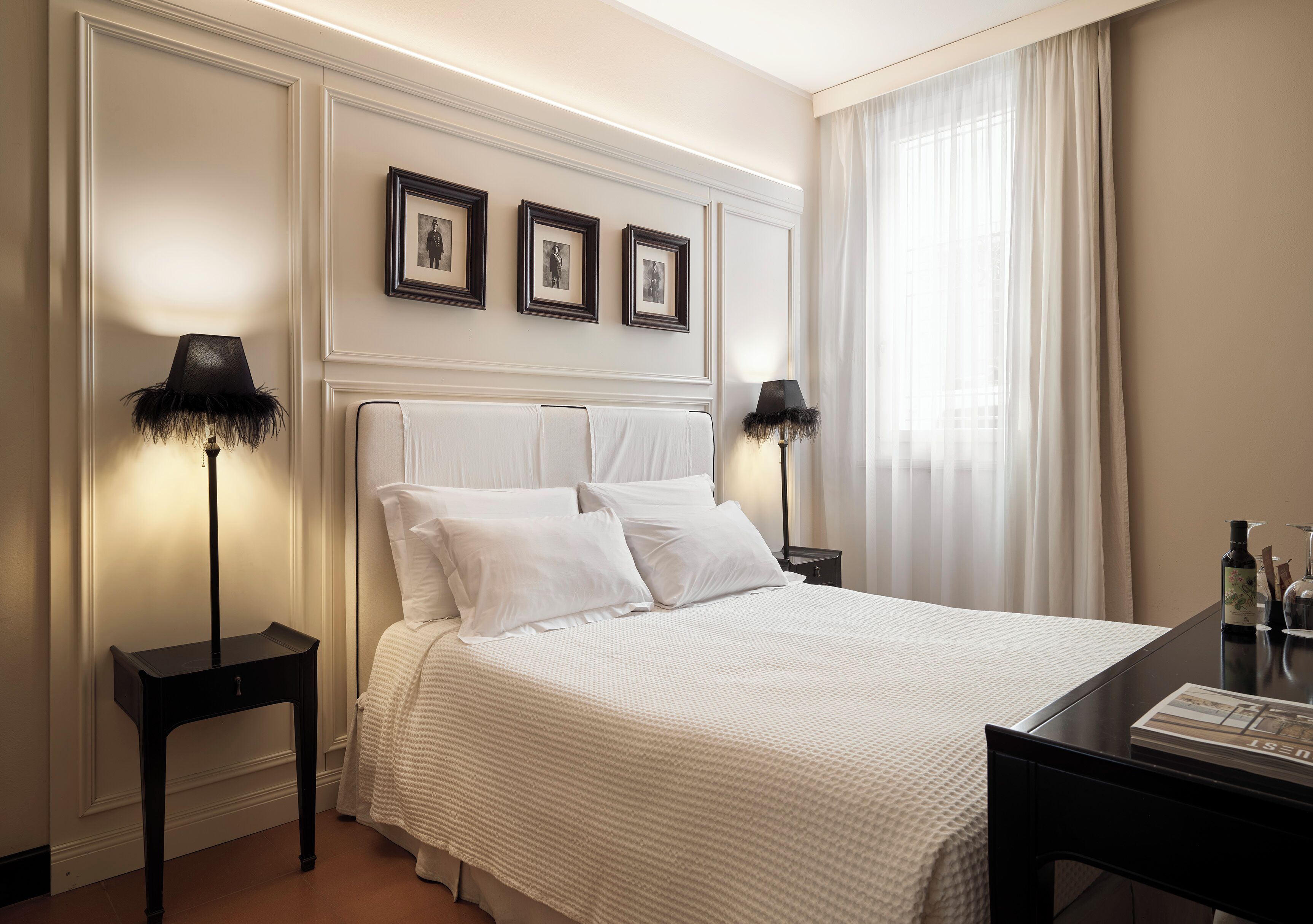 A hotel room with a large bed, two bedside tables, a nightstand, and a desk with a chair. There are three framed pictures on the wall above the bed.